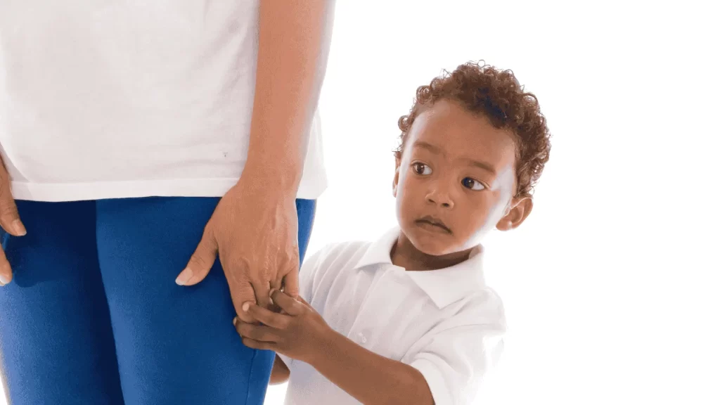 A young boy clings to his mother's leg, showing signs of separation anxiety around strangers