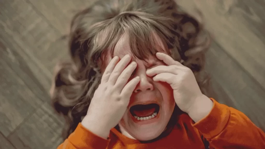 A toddler crying and throwing a tantrum as their parent leaves, displaying separation anxiety